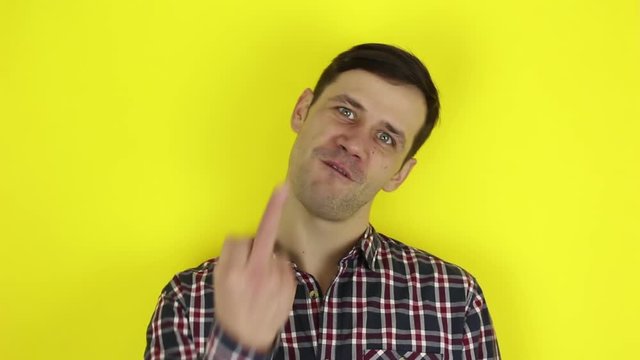 A funny, handsome guy shows indecent hand gestures. Portrait of a young guy, he expresses disgust and shows indecent hand gestures.Portrait on a yellow background.