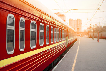 Naklejka premium Red metal train railway carriages with windows on a train station platform in the sunset light. Empty station, Odessa, Ukraine. Epidemic, no people on the platform