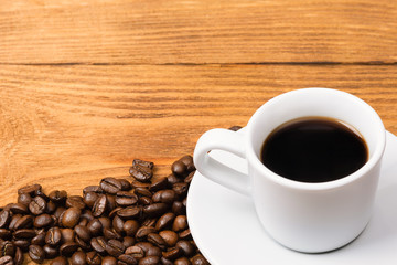 Freshly made coffee in a white cup surrounded by coffee beans on a wooden table. Fresh roasted coffee.