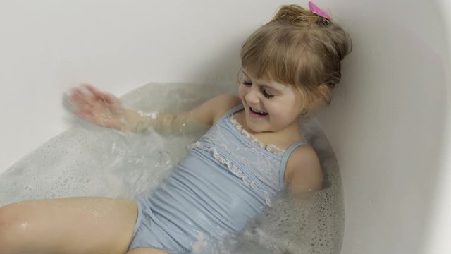 Cute blonde girl takes a bath in swimwear. Little child, 4 years old. Hygiene