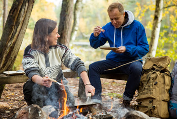 Man and woman making pancakes on campfire in forest on shore of lake, making a fire, grilling....