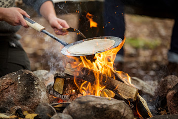 Man and woman making pancakes on campfire in forest on shore of lake, making a fire, grilling....