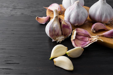 garlic cloves and bulb on wood serving board on dark wood background