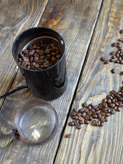 A coffee grinder with roasted coffee beans stands on a wooden table. coffee beans are scattered on the old wooden table top. vertical.