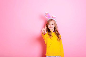Obraz na płótnie Canvas Beautiful baby girl blonde with Bunny ears points her finger up. Imitation touch- sensitive surface. Technology. Future. Happy Easter! Traditions, holidays, spring, the concept of religion.