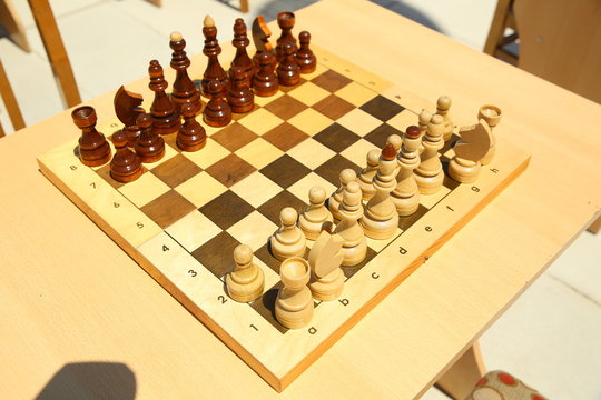 Yellow and brown photo with a picture of a chess Board pieces, Wooden pieces on a chess Board and emtye table . How to play wooden chess game. Chess board with yellow and brown figures .