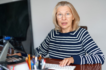 mature middle aged in glasses using laptop typing email working at home office, lady searching information on internet or communicating online