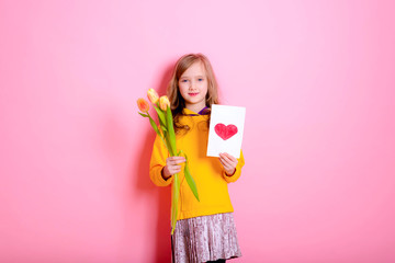 Happy Easter! Girl kid blonde in rabbit ears holding a card red heart, yellow tulips. Happy Mother's Day! International Women Day. Daughter's day.