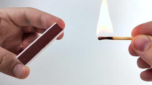 Men's hands light a match on the boxes. Macro video of a match head ignition. Concept of burning fire on a white background as a sign of the safe use of matches.