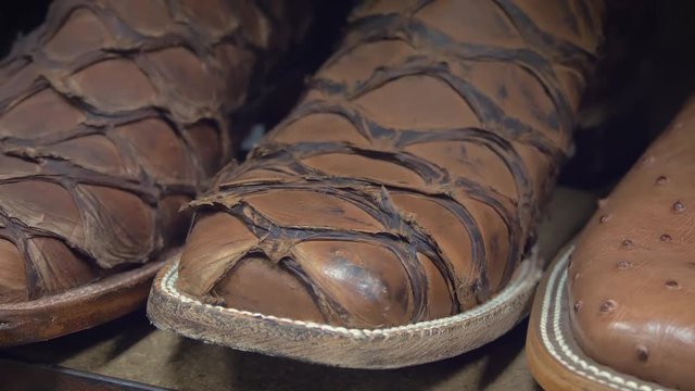 Detail shot of footwear in a row at traditional American cowboy boots. American-style boots from ostrich and buffalo leather. Close-up of new cowboy boots on shelf. Stylish leather western style boots