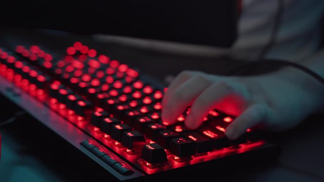 Closeup shot of professional gamer hands playing on keyboard in dark room. Kyber sport concept