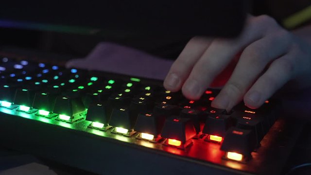 Closeup shot of professional gamer hands playing on keyboard in dark room. Kyber sport concept