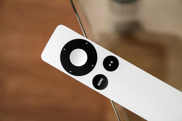 The modern grey steel Remote Control lies on a glass table.