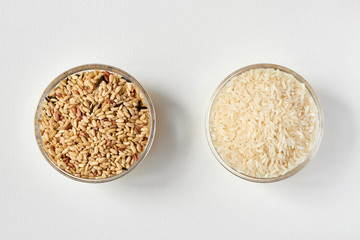 Raw brown rice and white rice in a transparent glass plate on white background. Problem of choice....