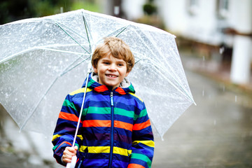 Beautiful little kid boy on way to school walking during sleet, rain and snow with an umbrella on...