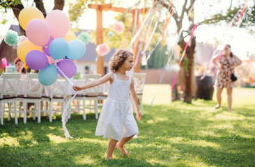 Portrait of small girl playing with balloons outdoors on garden party in summer.