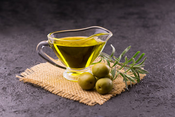 Olive oil in a transparent glass sauceboat, rosemary and olives on a black background. Close-up.
