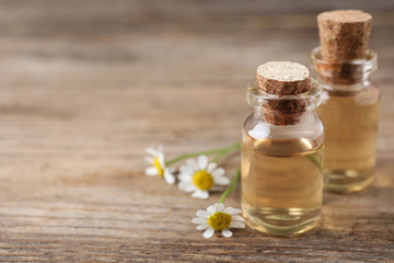Chamomile flowers and bottles of essential oil on wooden table, space for text
