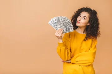 Fotobehang Portrait of a cheerful young woman holding money banknotes and celebrating isolated over beige background. © denis_vermenko