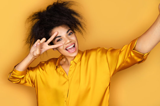 Cheerful girl taking selfie on the phone. Photo of african american girl on yellow background