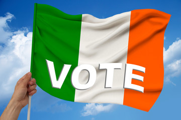 hand holds against the background of the sky with clouds the colored flag of Ireland on the texture of the fabric, silk with waves, close-up, with the word vote