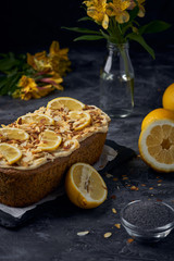 Vegan homemade lemon cake with poppy seeds and coconut sugar. White glaze with lemon slices and almonds. Selective focus. Dark photo style