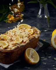 Vegan homemade lemon cake with poppy seeds and coconut sugar. White glaze with lemon slices and almonds. Selective focus. Dark photo style