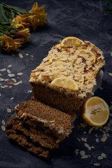Vegan homemade lemon cake with poppy seeds and coconut sugar. White glaze with lemon slices and almonds. Selective focus. Dark photo style
