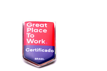 Clasp pin brooch with Great Place To Work written on a solid white surface background. TRANSLATION: 'CERTIFIED. BRAZIL'