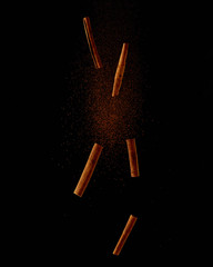 Obraz premium cinnamon sticks and powder falling on a black background. Food explosion, flight levitation. Creative concept