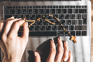 03/17/2020 Kiev, Ukraine: Catholic rosary and laptop lying on the table with a woman working at a computer and praying