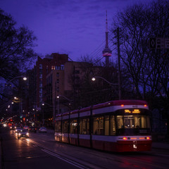 Obraz premium A streetcar on King street in Old Toronto district with cars, traffic lights, and street cars tracks glimmering in the darkness