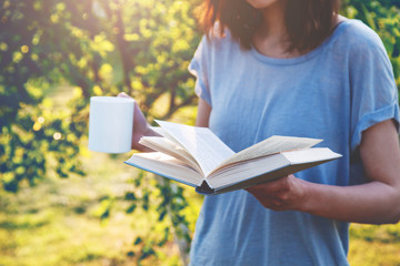 woman reading book and drinking coffee outside
