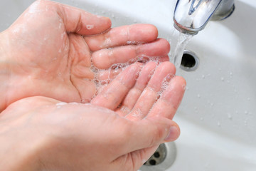Male hands under the tap with water over the sink in the bathroom.