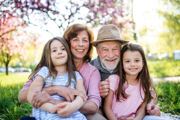 Senior grandparents with granddaughters sitting outside in spring nature.