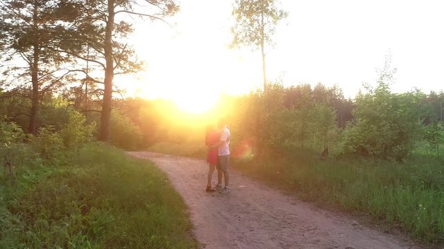 Warm evening sun light. Happy young couple hugging and kissing at sunset with amazing view pine forest