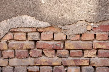 Closeup toned texture of falling off plaster from cracked brick wall. Old weathered painted background texture.