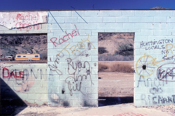 Graffiti / spray painted "tags" or names on abandoned cinder block store in Arizona desert with house trailer being towed in background.