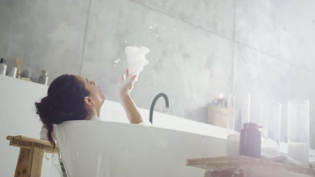Close up cheerful woman blowing foam in light bathroo imn slow motion.