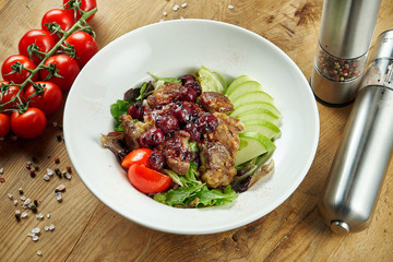 Salad with chicken liver, cherries, apples, lettuce and tomatoes in a white bowl on a wooden background. Close up