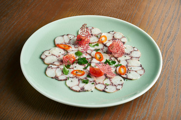 Tiradito is a Peruvian dish of raw octopus cut in the shape of sashimi with chilli pepper and cherry tomato on white plate on wooden background