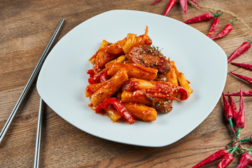 Tteok-bokki - traditional dish of korean cuisine, stir-fried rice cakes with pork ribs in white plate on wooden background. Close up. Selective focus