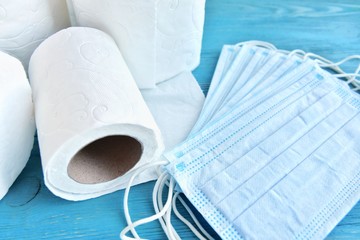roll of toilet paper and sterile protective masks with selective focus on blue wooden background. toilet paper and face mask for Covid-19 pandemic. Increased potential. high demand
