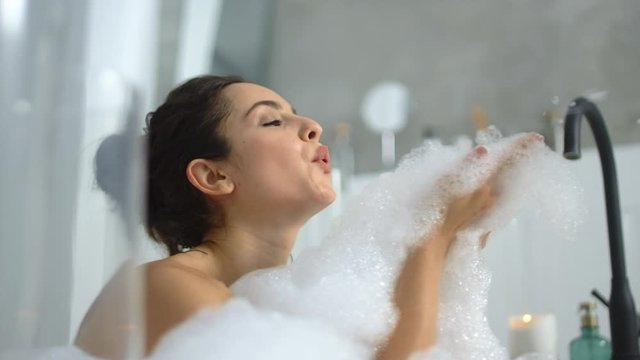 Closeup hot woman blowing foam at bathtub. Sexy girl playing with bubbles