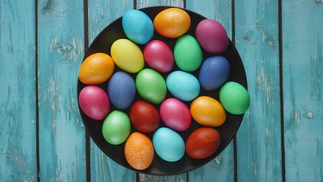 Top View Rotating Of Colorful Easter Eggs Lying On Black Plate On A Blue Wooden Background. Natural Daylight. Close-up 