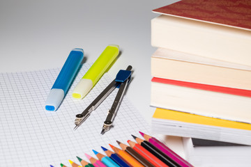 A compass with markers photographed on top of a checked sheet and a stack of books in the foreground.