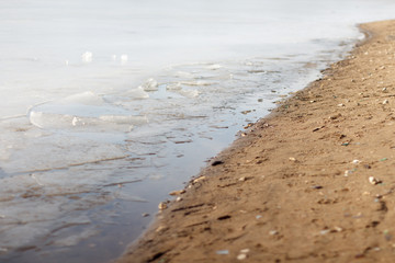 Fototapeta na wymiar Ice near the sandy shore, spring melting. Selective focus.