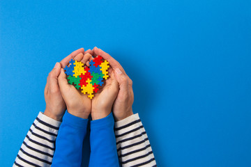 World autism awareness day concept. Adult and child hands holding puzzle heart on light blue background - obrazy, fototapety, plakaty