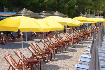 Yellow beach umbrellas and chaise for relax and comfort on sea coast in sunny day. Summer vacations and tourism concept. Paid service on waterscape beaches.