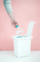 One person sorts recyclable materials on a pink background into a special bin for plastic bottles